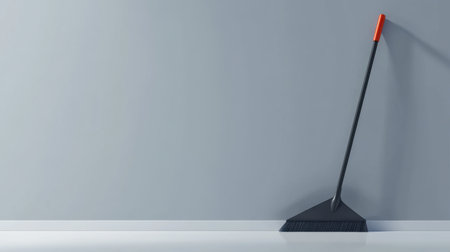 A sleek black broom with a red handle is positioned against a smooth gray wall, representing modern cleaning solutions and stylish home maintenance tools.の素材