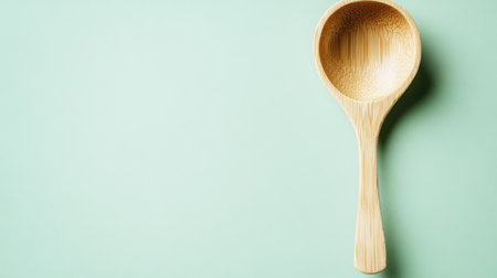 A beautifully crafted wooden cooking spoon rests on a soft mint green background, perfect for showcasing minimalist kitchen essentials. Ideal for culinary photography.の素材