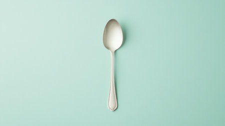 A simple silver spoon rests gracefully on a soft mint green background, perfect for culinary themes, home decor, or product displays.の素材
