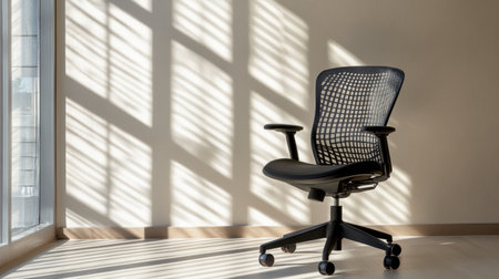 A sleek black office chair positioned in a bright workspace, with sunlight creating captivating patterns on the wall and floor, perfect for modern interiors.の素材