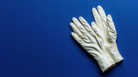 A pair of elegant white satin gloves lies gracefully on a rich blue background, ideal for showcasing fashion accessories and vintage styles in photography.の素材