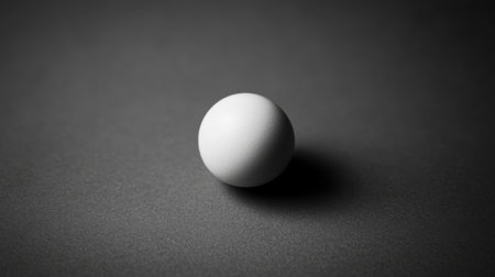 A striking minimalist image featuring a single white sphere set against a dark surface, casting a soft shadow. Ideal for artistic projects or conceptual themes.の素材