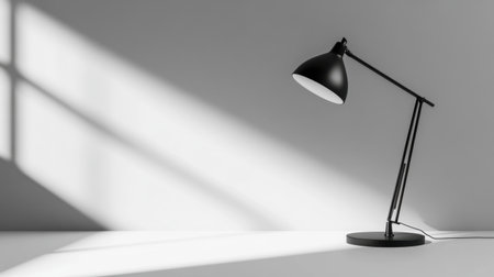 A sleek black desk lamp stands against a smooth grey wall, casting dynamic shadows. The minimalist design elevates any workspace while providing soft illumination.の素材