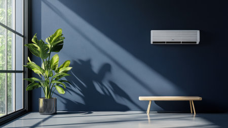 A minimalist interior scene featuring a sleek air conditioning unit, a lush green plant, and natural sunlight creating beautiful shadows on a blue wall.の素材