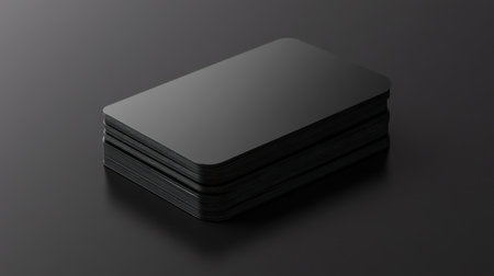 A sleek stack of minimalist black business cards rests on a dark surface, emphasizing style and elegance, ideal for modern branding presentations.の素材