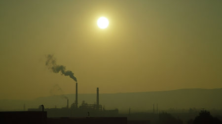 A striking image of an industrial landscape at dusk, showcasing factory smokestacks emitting pollution against a hazy sky, surrounded by natural beauty.の素材