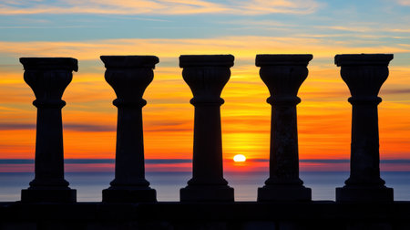 The image features a striking silhouette of five stone pillars against a vibrant sunset over the calm ocean horizon, creating a serene and tranquil atmosphere.の素材