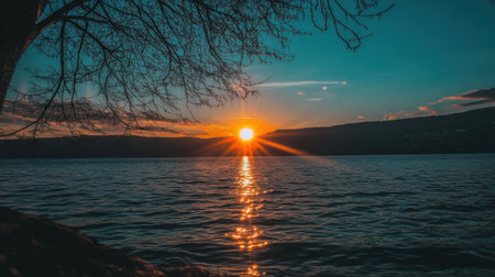 Experience a stunning sunset over a peaceful lake, with vibrant colors reflecting on the water's surface. A silhouette of a tree adds to the serene atmosphere.の素材