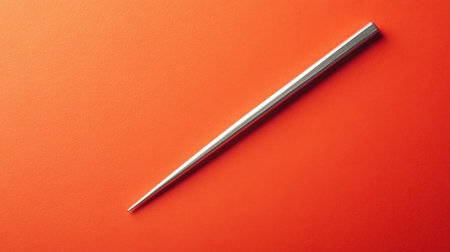 This image showcases a sleek metal object resting on a vibrant orange background, highlighting its smooth texture and minimalist design. Perfect for creative projects.の素材