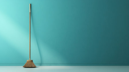 A vintage broom leans against a vibrant turquoise wall, showcasing a clean and minimalistic space illuminated by soft lighting and graceful shadows.の素材