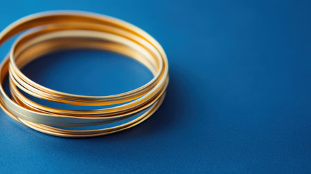 This image features a set of elegant golden bangles elegantly displayed against a vibrant blue backdrop. Perfect for fashion and jewelry concepts.の素材