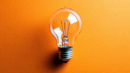 A vintage light bulb radiates warm light against a vivid orange backdrop, providing an aesthetic appeal perfect for creative design ideas and concepts.の素材