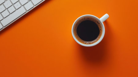A stylish white cup of freshly brewed black coffee perched on a vibrant orange background, with a sleek computer keyboard. Ideal for conveying productivity and comfort.の素材