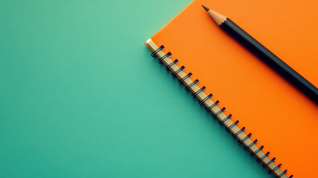 A vibrant orange notebook with a spiral binding lies alongside a black pencil on a soft turquoise surface, perfect for creativity and organization.の素材