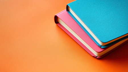 This image features colorful notebooks stacked against a vibrant orange background, ideal for showcasing creativity, education, and artistic expression.の素材