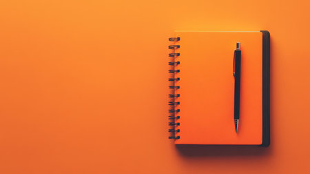 A flat lay image featuring a vibrant orange notebook paired with a sleek pen, set against a flat color background, perfect for creative projects and organization.の素材