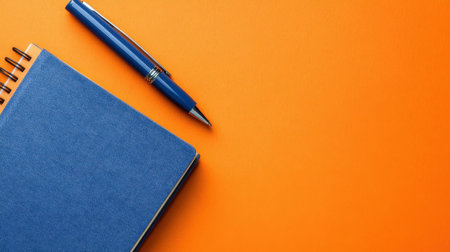 A vibrant arrangement featuring a blue notebook and blue pen atop an orange background, ideal for inspiring creativity and organization in any workspace.の素材