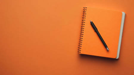 A vibrant orange notebook sits on a matching background, accompanied by a sleek black pen. Perfect for highlighting creativity in educational or office settings.の素材