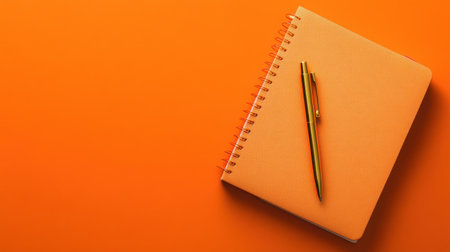 A vibrant orange notebook paired with stylish pens rests on a matching background, perfect for creative work, organization, and modern aesthetics.の素材