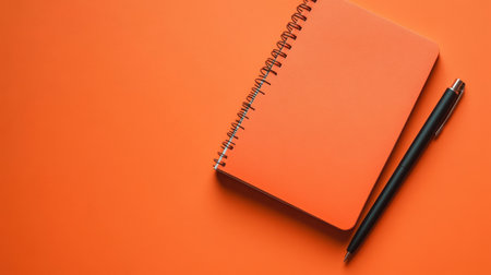 A vibrant orange notebook paired with a sleek black pen rests on a bright orange background, creating an inviting atmosphere for writing and planning.の素材