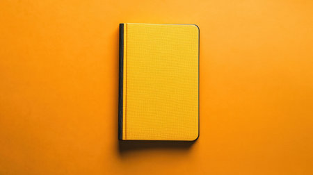 A vibrant yellow notebook rests on a bright orange background, creating a striking visual contrast. Perfect for creative projects, note-taking, and planning.の素材