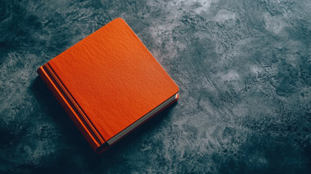 An orange notebook elegantly positioned on a grey textured surface, showcasing a modern aesthetic perfect for creative projects and organizational tasks.の素材