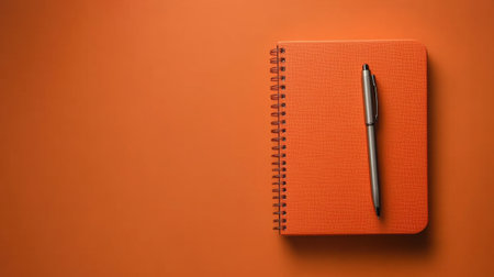 A vibrant orange notebook rests alongside a sleek pen on a matching background. Perfect for inspiring creativity, note-taking, and organization.の素材