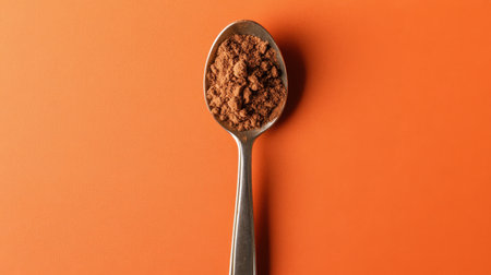 A silver spoon filled with rich cocoa powder is artistically presented against a bright orange background, perfect for culinary themes and food photography.の素材