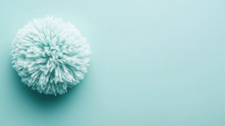 A soft mint green pom pom rests on a light blue background, showcasing its fluffy texture and vibrant color, perfect for creative projects and design inspiration.の素材