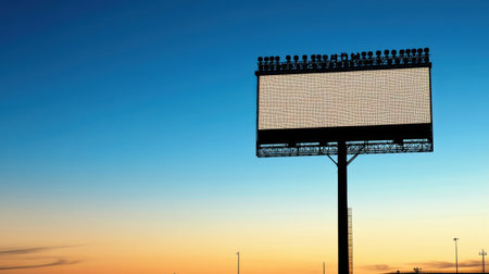 A striking image of a blank digital billboard set against a colorful sunset sky. The scene captures an evening atmosphere with illuminated lights and a clear horizon, perfect for representing outdoor advertising.の素材