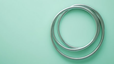 Two sleek silver metal rings rest elegantly on a soft mint green background, creating a visually appealing composition ideal for design and artistic projects.の素材