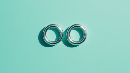 A pair of sleek silver rings lies on a vibrant mint background, showcasing modern elegance and simplicity, ideal for jewelry and fashion promotions.の素材