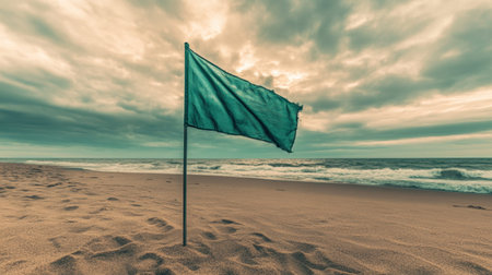 A solitary green flag stands prominently on a sandy beach, surrounded by a picturesque view of the ocean waves and a dramatic cloud-filled sky, evoking serenity.の素材