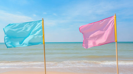 Two colorful flags, one blue and one pink, stand on a beach, swaying gently in the wind. The serene ocean and bright sky create a tranquil atmosphere.の素材
