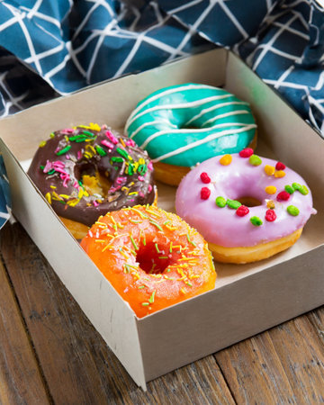 Colorful glazed donuts in a box on a wooden tableの素材
