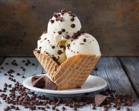 Chocolate ice cream in waffle cone with chocolate chips on wooden backgroundの素材