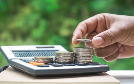 The businessman's hand is putting coins or money in a financial calculator. Saving money for investmentの写真素材