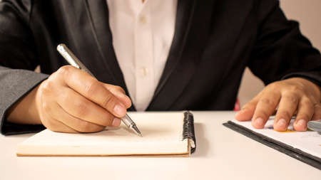 Close-up pictures of a man who wrote a spiral notebook on the table with a coffee mug and writer's...