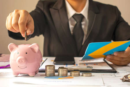 A businessman holds a coin on the piggy bank to save money for investment ideas, savings and sustainable investments.の写真素材