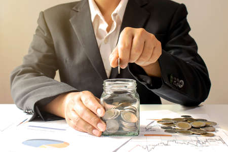 Business woman holding a coin in a money jar and window light money saving idea.の写真素材