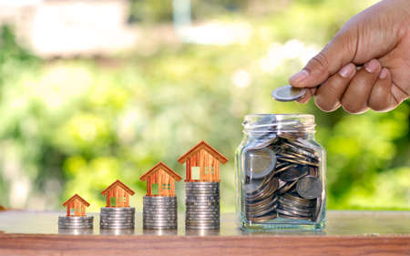 The hands of the man who holds the money in a bottle to save money, including a house at the top of the coin, money saving ideas for buying a house.の写真素材