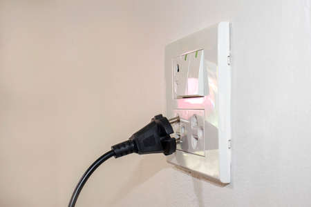 The dangers of using electricity in your home or office include a black plug that is not completely plugged into the white wall.の写真素材