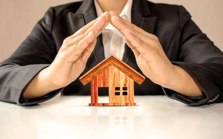 The model of a brown wooden house with the hands of a businessman surrounds the concept of investing in real estate and saving money on home purchases.の写真素材