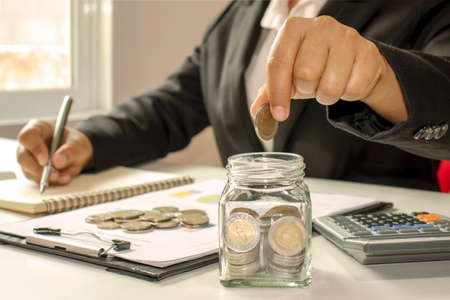 Close-up of a business woman holding a coin in a piggy bank, as well as writing a financial record, a concept for saving money.の写真素材