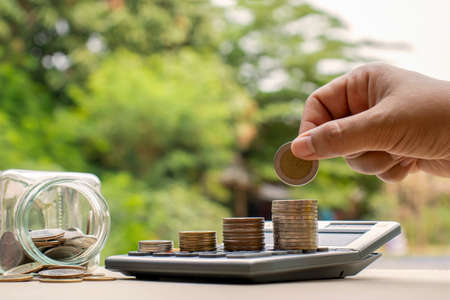 Human hands place money coins and piles of coins on a calculator, including money jars, financial concepts and business growth.の写真素材