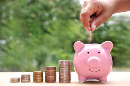 Close-up of a woman putting a coin in a piggy bank, including a coin stack, saving ideas and financial growth.の写真素材