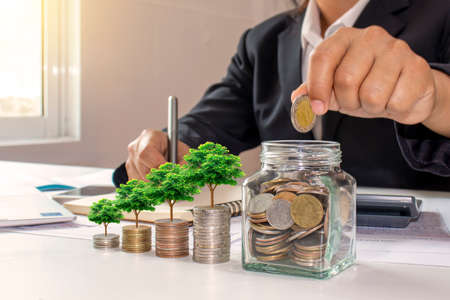 Business women who are putting coins in a bottle of money, including growing saplings on coins or money, ideas for saving money and financial growth.の写真素材