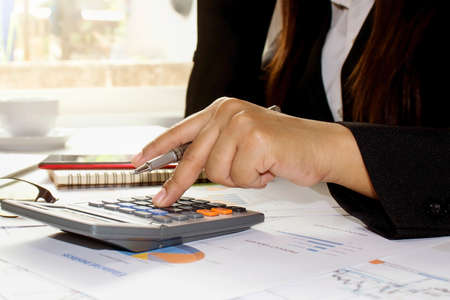 Business women use calculators to calculate annual reports, including laptops and notebooks on wooden desks for work, work ideas, and account management.の写真素材