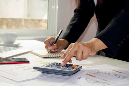 Close-up of women using calculators to create accounting reports by the window in their own homes, cost calculation concepts, and work at home concepts.の写真素材
