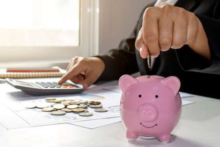 Business women who hold coins in a piggy bank closely, including pressing a calculator for money saving ideas.の写真素材